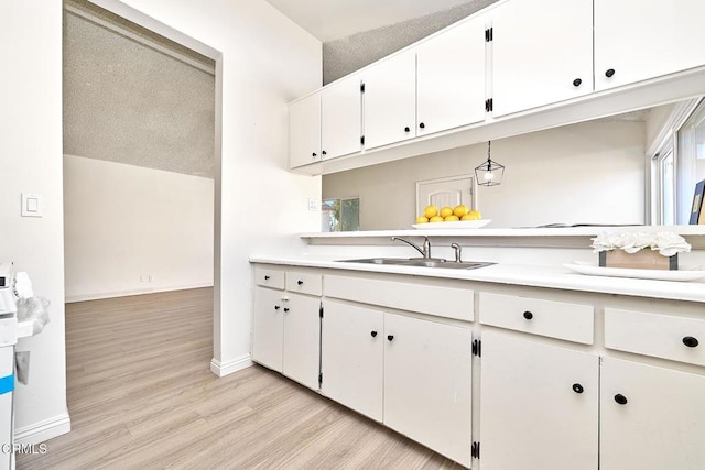 kitchen with baseboards, white cabinets, light countertops, light wood-style floors, and a sink