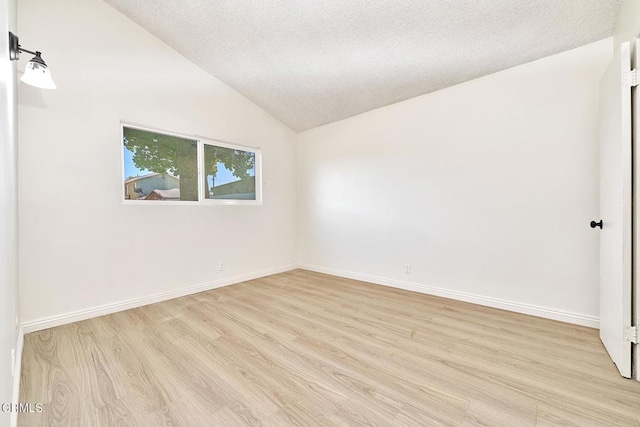 empty room with light wood-style floors, lofted ceiling, a textured ceiling, and baseboards