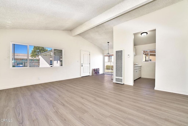 unfurnished living room with vaulted ceiling with beams, a textured ceiling, baseboards, and wood finished floors