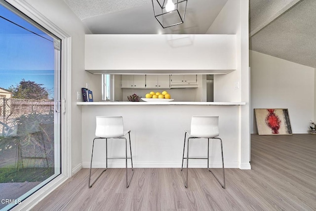 kitchen with light countertops, a textured ceiling, wood finished floors, a peninsula, and a kitchen bar