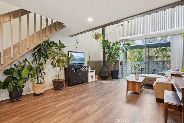 living room with stairway, wood finished floors, a wood stove, and baseboards