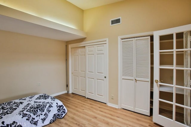 bedroom featuring baseboards, visible vents, light wood-style flooring, and two closets