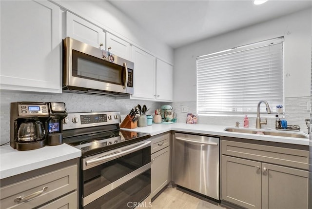 kitchen featuring gray cabinetry, a sink, stainless steel appliances, light countertops, and decorative backsplash