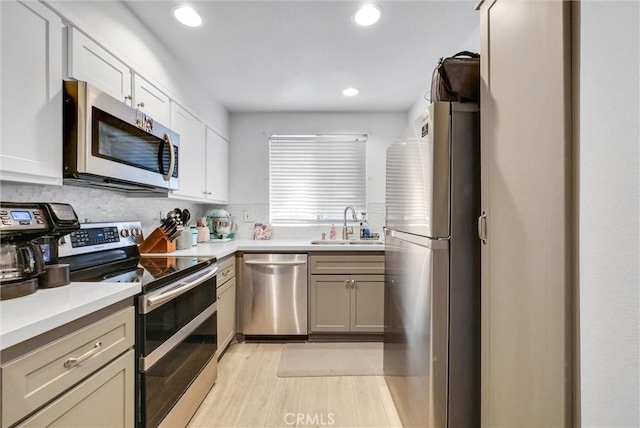 kitchen with light wood finished floors, backsplash, light countertops, stainless steel appliances, and a sink