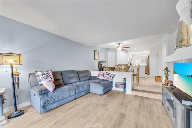 living room featuring baseboards, light wood-type flooring, and ceiling fan