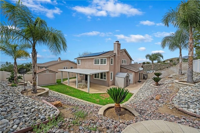 back of property with solar panels, stucco siding, a fenced backyard, an outbuilding, and a patio