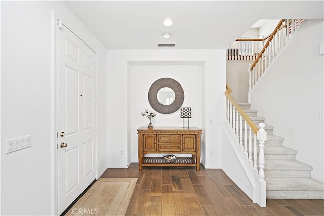 entrance foyer with dark wood finished floors, visible vents, stairs, and baseboards