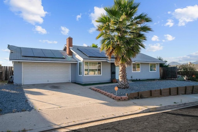 ranch-style house with driveway, a chimney, an attached garage, fence, and roof mounted solar panels