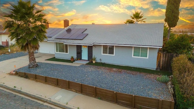 view of front of property featuring stucco siding, an attached garage, roof mounted solar panels, fence, and driveway