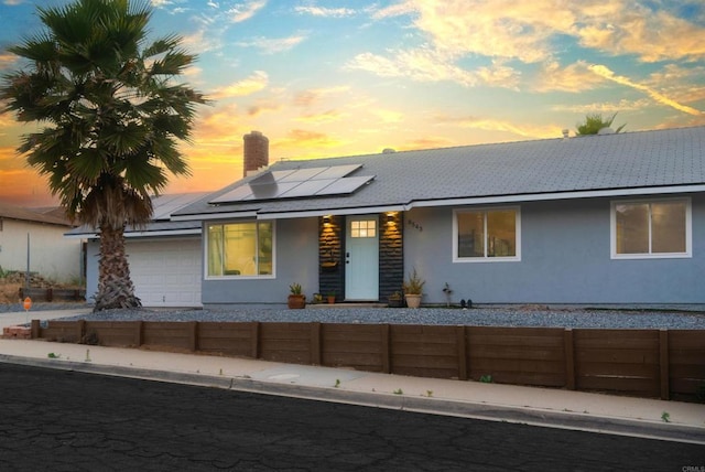 view of front facade with a chimney, stucco siding, an attached garage, roof mounted solar panels, and fence