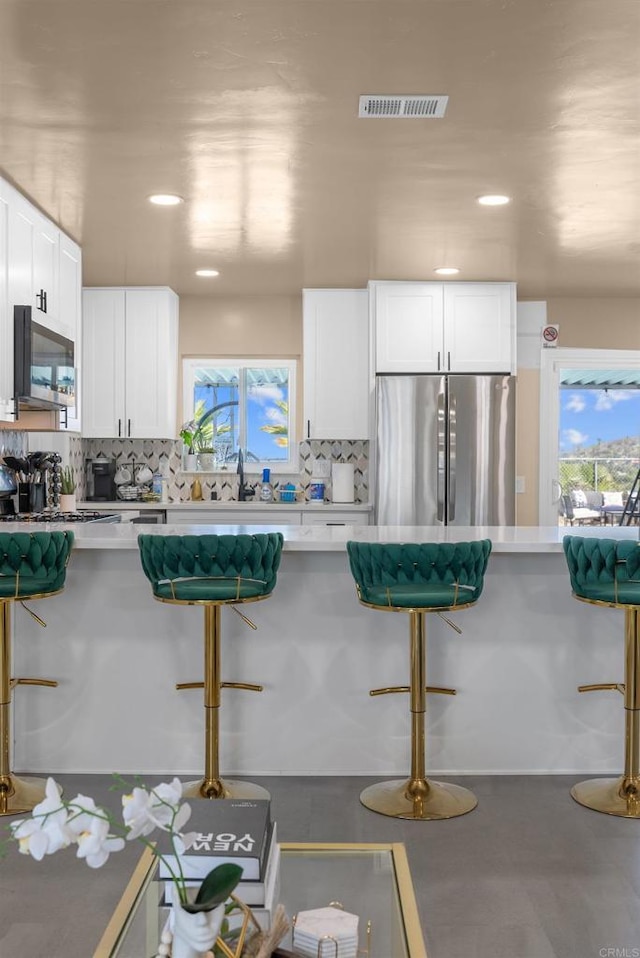 kitchen with visible vents, appliances with stainless steel finishes, decorative backsplash, and a breakfast bar area