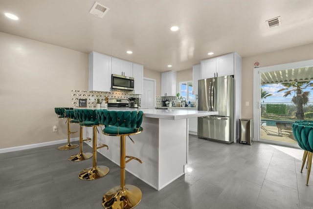 kitchen with white cabinets, a kitchen breakfast bar, a peninsula, stainless steel appliances, and backsplash