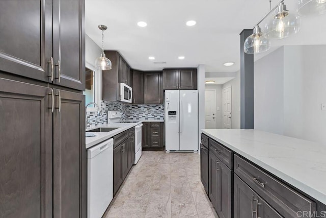 kitchen with tasteful backsplash, dark brown cabinetry, light stone counters, white appliances, and a sink