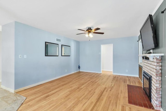 unfurnished living room with light wood-type flooring, visible vents, a fireplace, baseboards, and ceiling fan