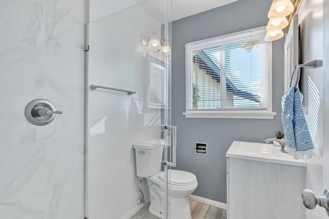 bathroom with vanity, wood finished floors, baseboards, a tile shower, and toilet