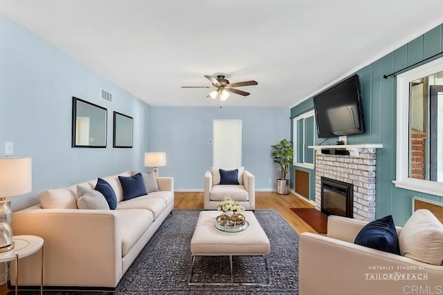 living area featuring visible vents, a brick fireplace, baseboards, light wood-type flooring, and a ceiling fan