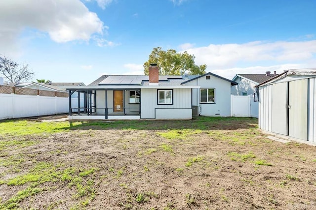 back of house featuring an outbuilding, roof mounted solar panels, a fenced backyard, a chimney, and a patio area