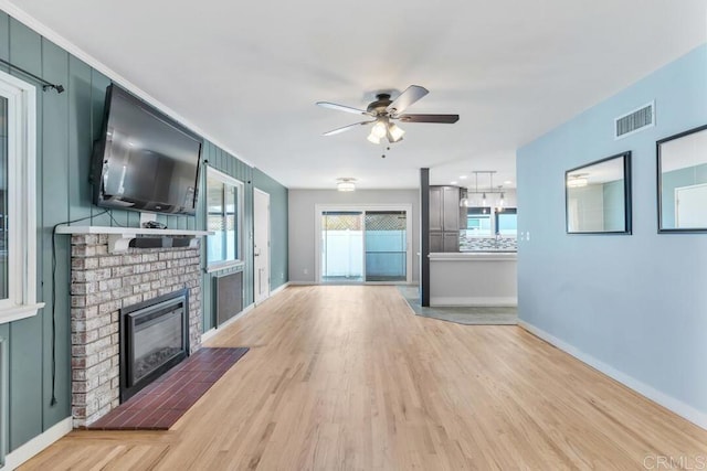 unfurnished living room featuring visible vents, light wood-style flooring, baseboards, a brick fireplace, and ceiling fan