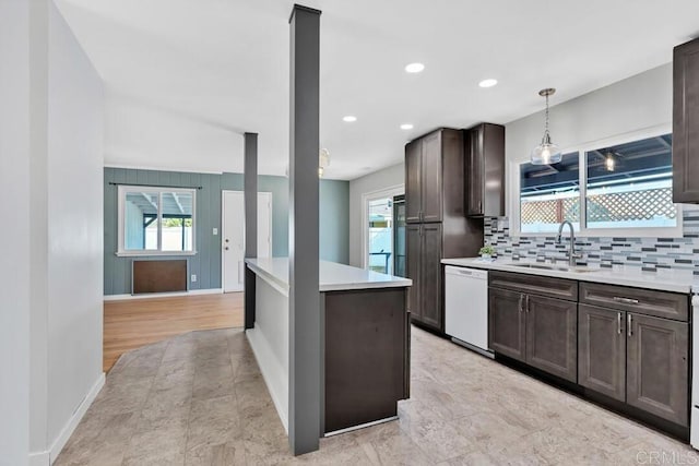 kitchen with white dishwasher, a sink, light countertops, dark brown cabinets, and backsplash