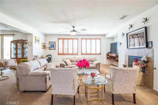 living area featuring visible vents, a tiled fireplace, carpet floors, a textured ceiling, and a ceiling fan