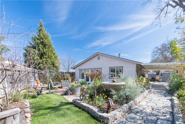 rear view of house with stucco siding, concrete driveway, a lawn, fence, and a carport