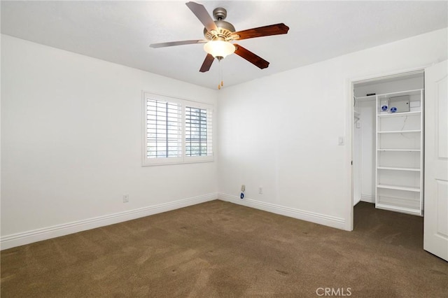 unfurnished bedroom featuring dark colored carpet, a closet, a spacious closet, ceiling fan, and baseboards