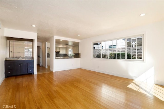 unfurnished living room featuring recessed lighting, light wood-type flooring, a sink, and baseboards