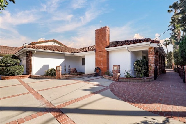 view of front facade featuring a tile roof, a chimney, and stucco siding