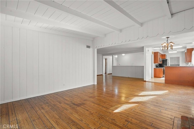 unfurnished living room featuring light wood finished floors, visible vents, a chandelier, beamed ceiling, and baseboards