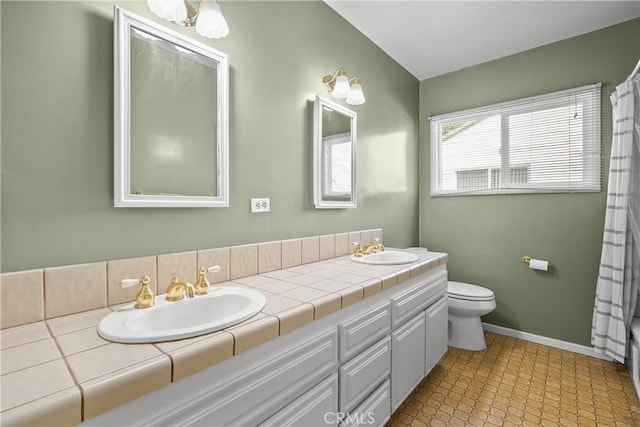 bathroom with baseboards, a sink, toilet, and double vanity