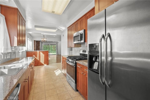 kitchen featuring light tile patterned floors, stainless steel appliances, tasteful backsplash, brown cabinetry, and a sink