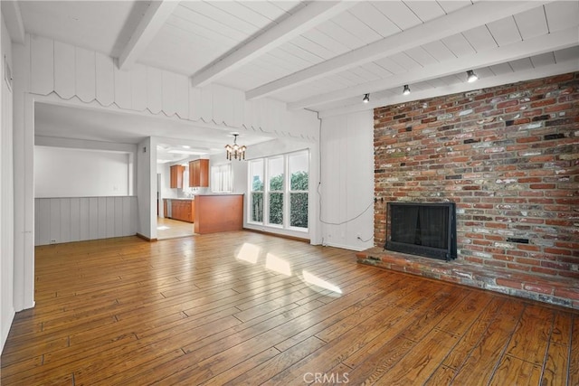 unfurnished living room featuring a brick fireplace, beam ceiling, a chandelier, and hardwood / wood-style flooring