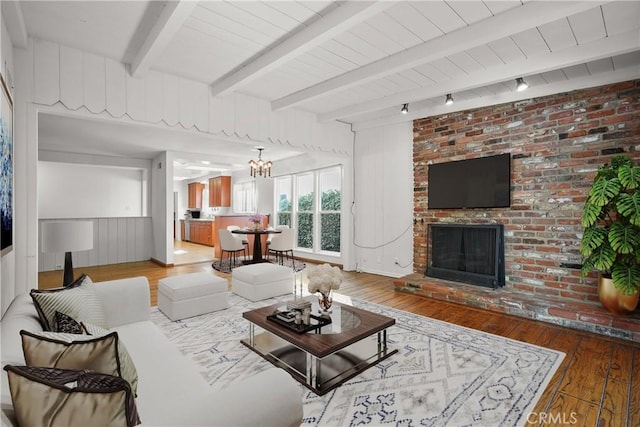 living area with a brick fireplace, beam ceiling, and wood finished floors