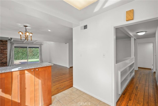 kitchen featuring a chandelier, light stone counters, light tile patterned flooring, visible vents, and brown cabinetry