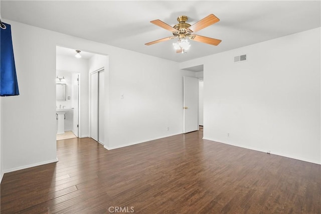 empty room featuring dark wood-style floors, ceiling fan, visible vents, and baseboards