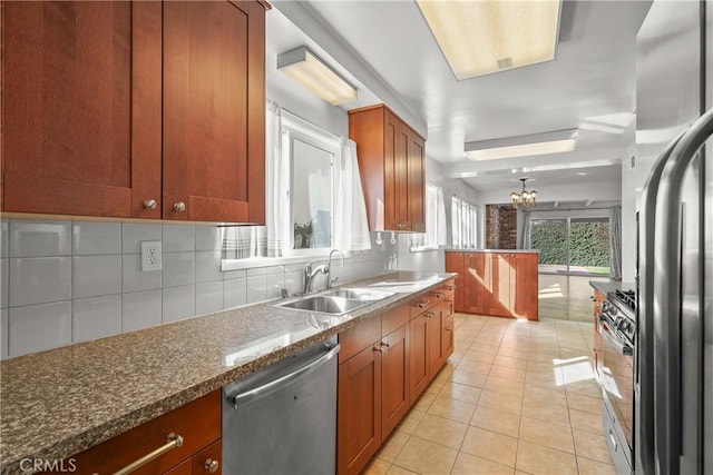 kitchen with light tile patterned floors, stainless steel appliances, backsplash, brown cabinetry, and a sink