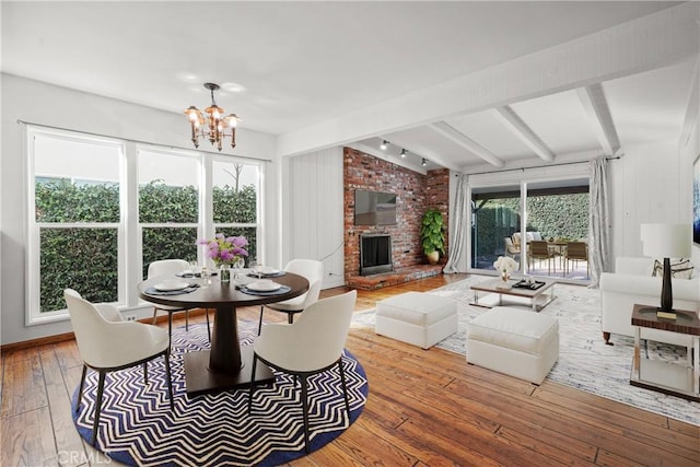 dining area with a chandelier, lofted ceiling with beams, a brick fireplace, and hardwood / wood-style flooring