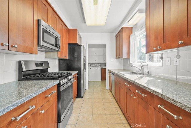 kitchen featuring light tile patterned floors, stainless steel appliances, brown cabinetry, washing machine and dryer, and a sink