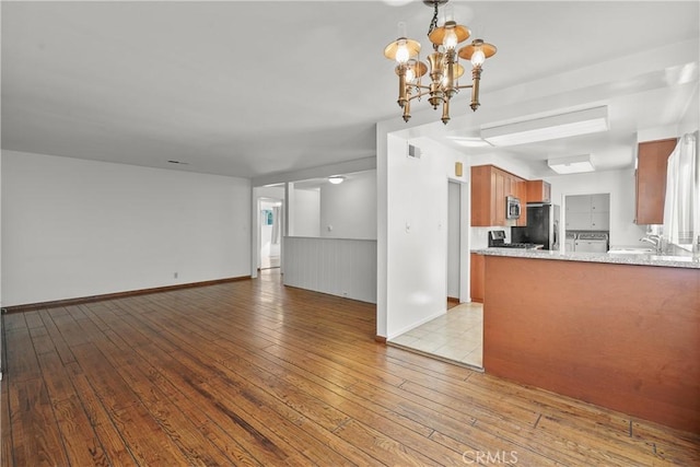 unfurnished living room with light wood-style floors, visible vents, a chandelier, and baseboards