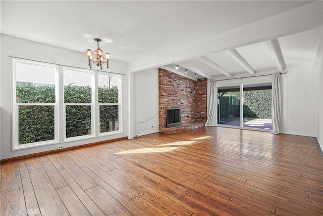 unfurnished living room with a chandelier, lofted ceiling with beams, a fireplace, baseboards, and wood-type flooring