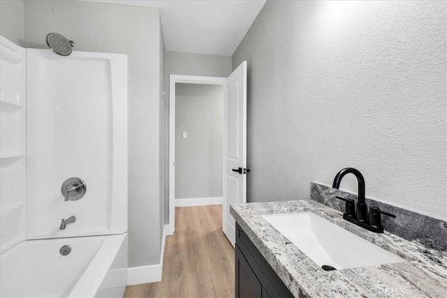 bathroom with baseboards, a textured wall, wood finished floors, vanity, and shower / bathing tub combination