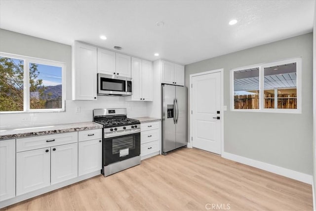 kitchen featuring appliances with stainless steel finishes, stone countertops, light wood-style floors, white cabinetry, and baseboards