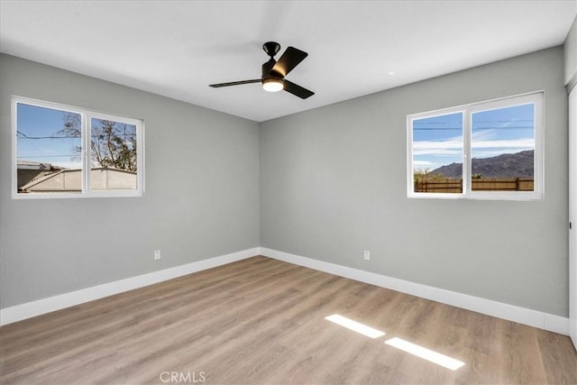 spare room with a ceiling fan, plenty of natural light, baseboards, and wood finished floors