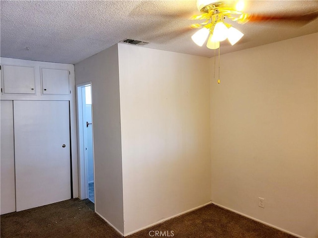 empty room featuring visible vents, dark carpet, and a textured ceiling