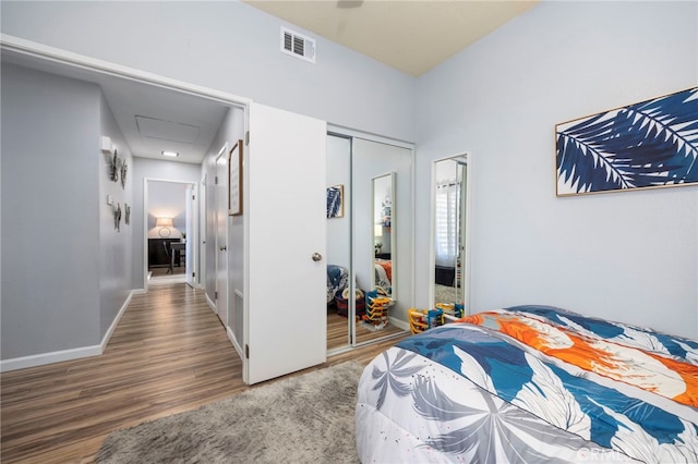 bedroom featuring wood finished floors, visible vents, baseboards, a closet, and attic access