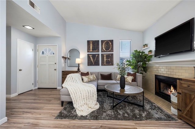 living room featuring a fireplace, lofted ceiling, visible vents, wood finished floors, and baseboards