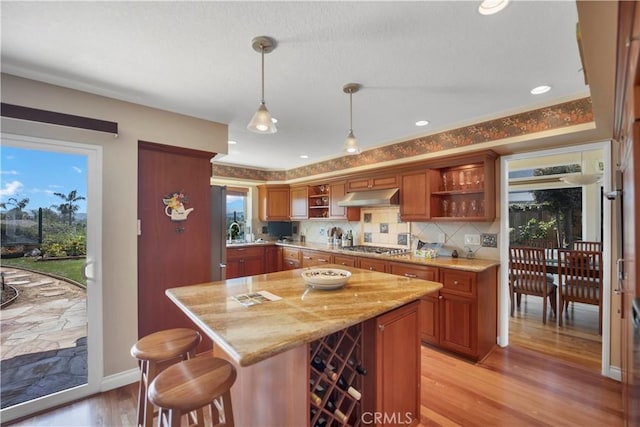 kitchen featuring pendant lighting, open shelves, backsplash, light wood-type flooring, and under cabinet range hood