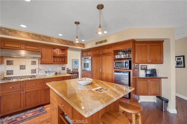 kitchen with brown cabinets, under cabinet range hood, appliances with stainless steel finishes, and open shelves