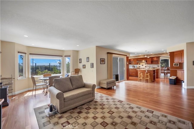 living area featuring light wood-style floors, baseboards, a textured ceiling, and recessed lighting