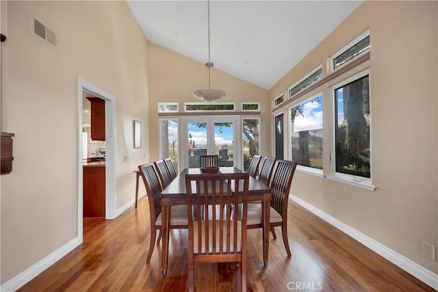 dining space featuring high vaulted ceiling, baseboards, visible vents, and wood finished floors